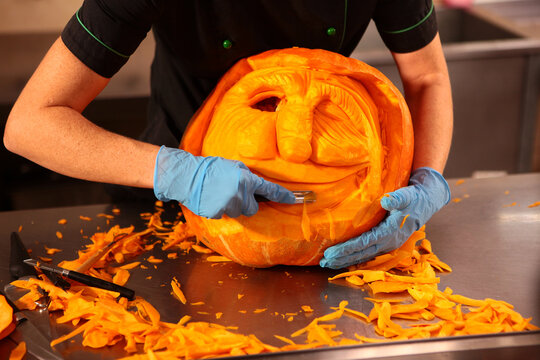 Pumpkin carving. Master carves scary face out of pumpkin. Artistic slicing of vegetables for Halloween decorations. Decorating festive tables and creating spectacular compositions for banquets