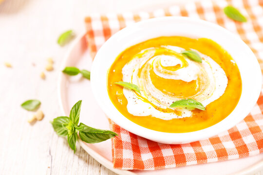 Creamy pumpkin soup with cream swirl and fresh basil in bowl