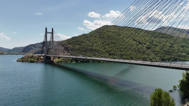 Aerial view along the bridge span over blue water and green mountain hills