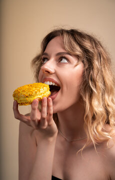 Young woman enjoying a sweet yellow donut reaching for a bite, looking up with craving expression and open mouth