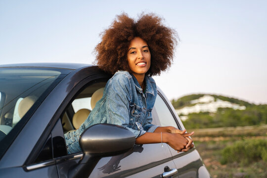 Young woman during road trip, leaning out of window