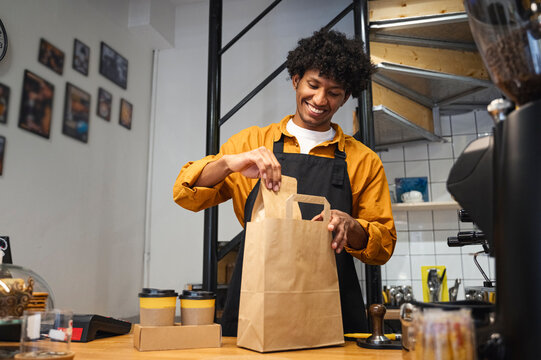 Smiling barista packing takeaway order at coffee shop