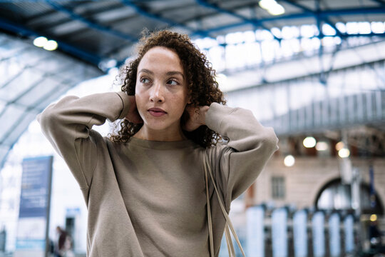 Young woman with hand in hair standing at train station