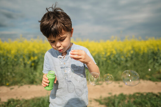 Child blowing soap bubble in yellow flower field during summer