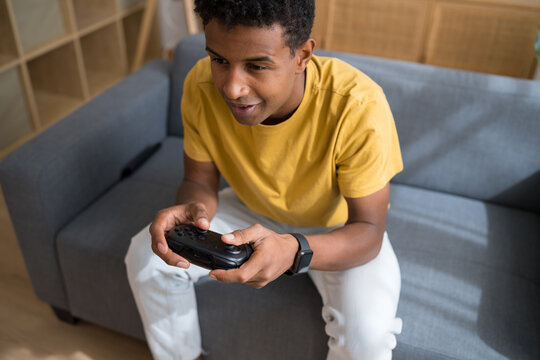 Man gaming on sofa with controller in yellow shirt indoors