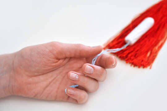 Woman holds a tampon with a red tassel symbolizing menstruation