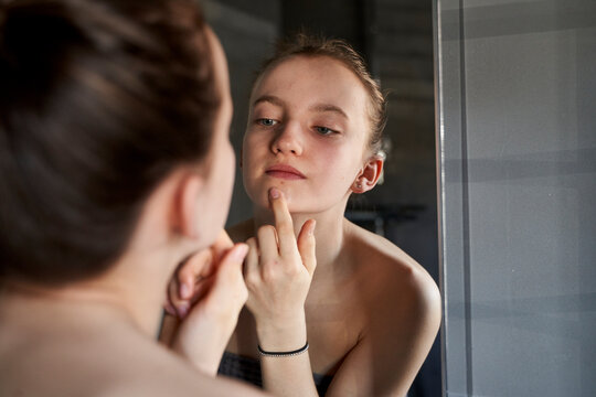 Mirror image of girl applying face cream in bathroom