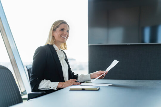 Happy female professional sitting with documents at desk in office