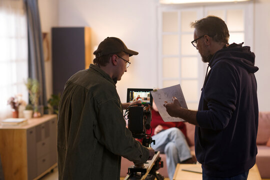 Two men operate a film camera and direct a scene indoors
