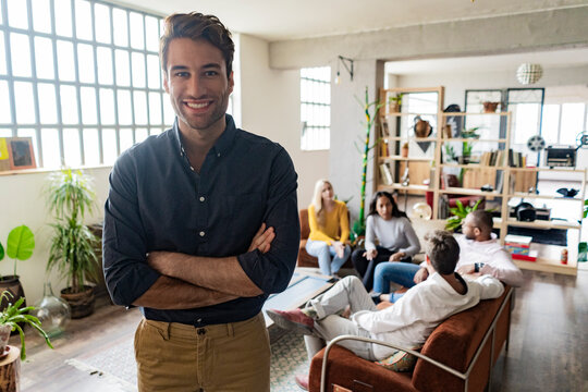 Portrait of smiling young businessman with coworkers in background in loft office
