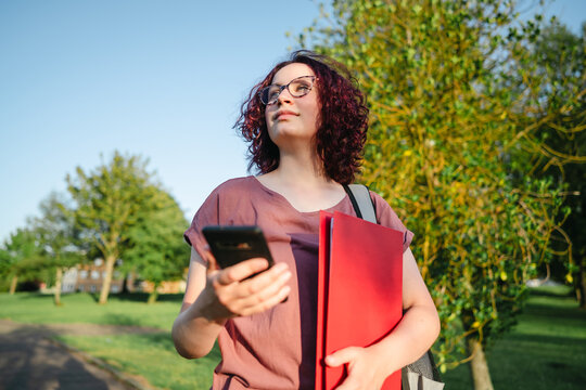 A female student holds a smartphone and a red folder outdoors