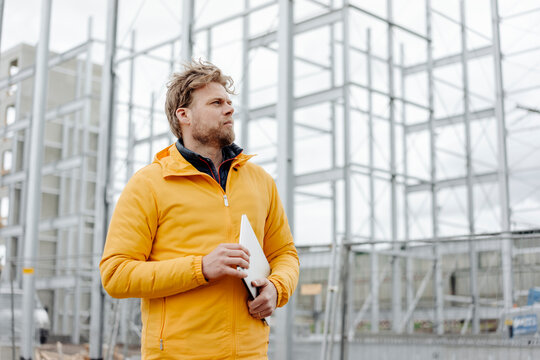 Man holding laptop, construction site in the background