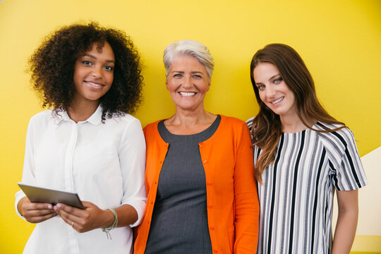 Group picture of three smiling women standing in front of a yellow wall
