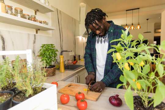 Young man cutting yellow chili pepper in kitchen