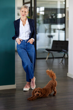 Confident businesswoman stands in the office with her stretching dog