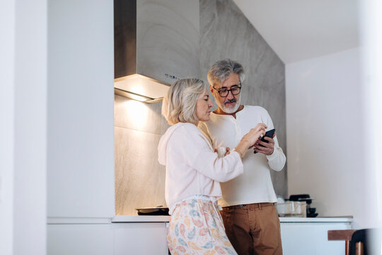 Mature couple using cell phone in kitchen at home