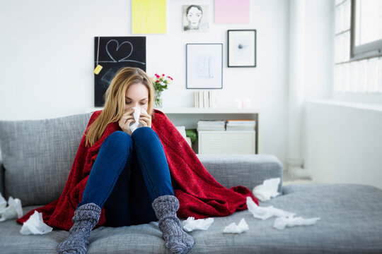 Sick woman blows her nose with a tissue on the sofa indoors