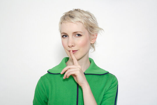 Smiling blonde looking at camera making silence gesture