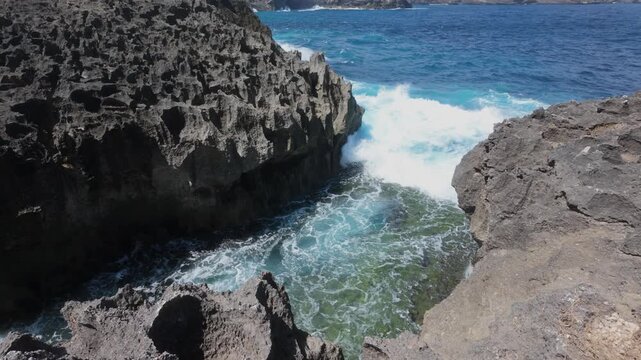 Waves crash onto Angel's Billabong in slow motion. The camera moves forwards. Angel's Billabong is a stunning natural infinity pool and limestone rock formation on the western coast of Nusa Penida, Ba