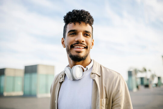 Smiling young man with curly hair wearing wireless headphones