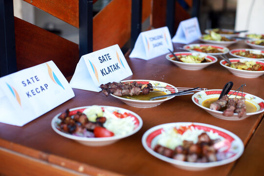 Various traditional Indonesian mutton dishes including Sate Klatak and Sate Kecap served with name tags on a wooden table. Asian culinary cuisine, authentic food culture concept.