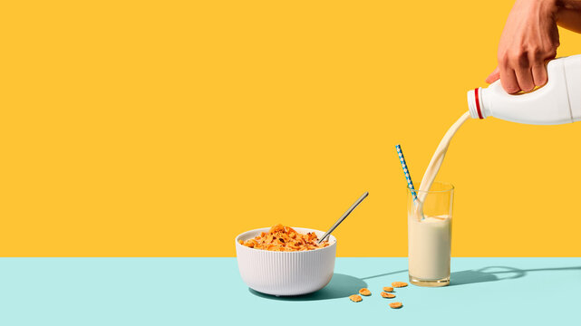 Milk poured into glass beside breakfast cereal on colorful studio background. Concept of healthy breakfast, dairy nutrition, morning routine, family meals, and food advertising.