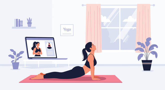 Active young woman performs a cobra yoga pose on a pink mat while watching a video lesson on her laptop screen.