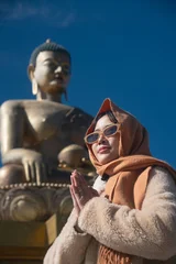 Fotobehang Lotusbloem An asian woman standing at magnificent large Buddha statue in a sitting posture on a lotus throne, set against a clear blue sky in Bhutan  © Oil And Den