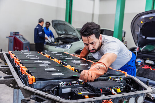 Confident electric vehicle technician smiling beside a high-voltage battery pack during maintenance in a modern EV service center.
