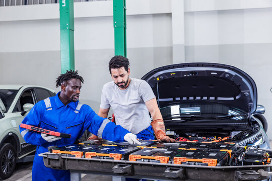 Professional EV technicians performing a detailed inspection of high-voltage battery modules in a modern electric vehicle service workshop. 