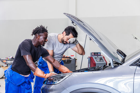 Two professional EV technicians working together to troubleshoot a complex electrical issue in a modern electric vehicle service center. 