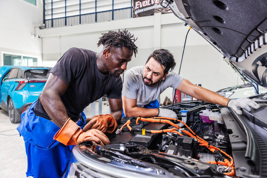 Professional EV technicians collaborating to diagnose and resolve an electrical problem in a modern electric vehicle service workshop.r