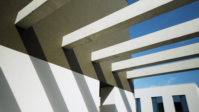 Modern architectural concrete beams casting geometric shadows on a building facade under blue sky