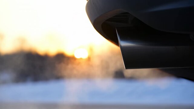 Close-up of vehicle exhaust tailpipe with rising steam backlit by low winter sun over snowy ground, with exhaust, tailpipe, vehicle, car detail, showing metal, chrome, bumper, vapor context