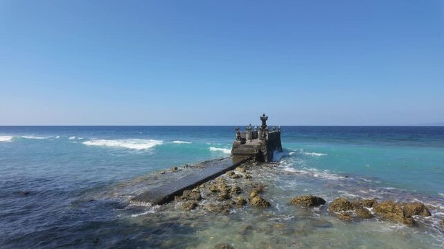 Small Balinese pelinggih sea shrine. On the coast of Nusa Penida, Bali. A small shrine sits in the Bali sea. Slow motion waves, turquoise water. Balinese culture and spirituality. 