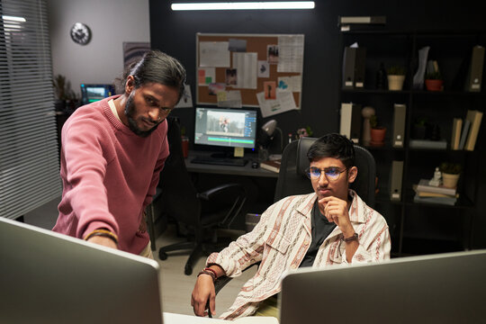 Medium shot of diverse men reviewing content on desktop monitors in creative office, collaborating on postproduction workflow. Ideal for teamwork, media production, mentoring