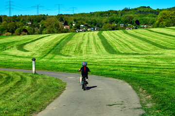 Fototapeta premium Kind mit Fahrradhelm fährt auf einem Feldweg an einer gemähten Wiese vorbei in Breitenborn, Main-Kinzig-Kreis, Hessen