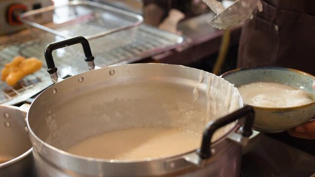 Chef Serving Hot Rice Porridge From Large Metal Pot Into Bowl