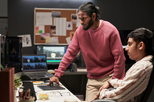 Two male coworkers reviewing video editing project on desktop and laptop in creative office, collaborating on postproduction workflow. Ideal for media teamwork or content studio marketing