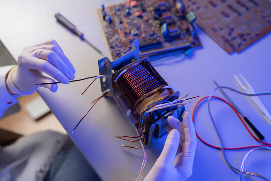 A person repairs a motor by connecting wires while tools and circuit boards are on the table in a workshop