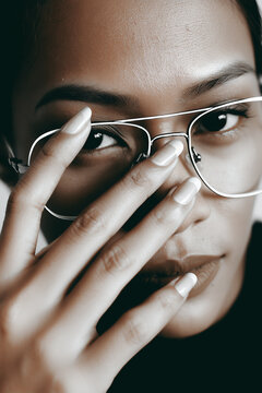 Close up portrait of a young woman adjusting her wire-frame aviator glasses with her manicured hand.