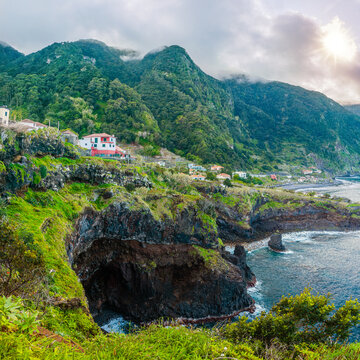 Wild Atlantic waves crashing into dark volcanic rock formations forming unique natural tidal pools on the coast of Seixal, Madeira, Portugal.