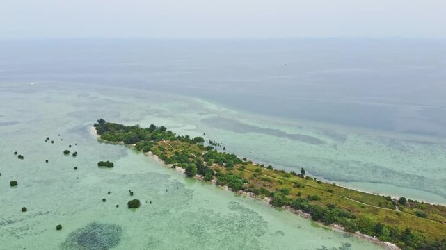 Aerial view of a tropical island archipelago surrounded by clear turquoise sea and coral reefs. Drone shot of an island strip with green trees in the ocean. Pari island in Indonesia 