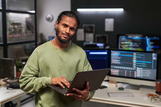 Portrait of young web engineer holding laptop and working in software development office, suggesting coding workflow and digital career. Useful for tech hiring, IT services, startup marketing