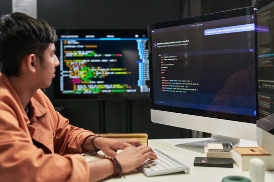 Young programmer coding at desktop computer, reviewing interface prompts and software script on multiple screens. Ideal for web development, AI workflow, tech training marketing