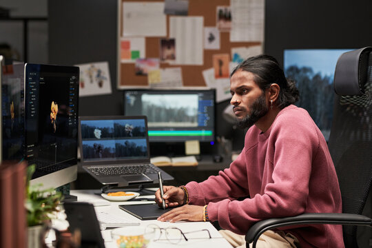 Young man editing video at workstation, using pen tablet and multiple screens for postproduction workflow. Ideal for creative agency, content marketing, media production