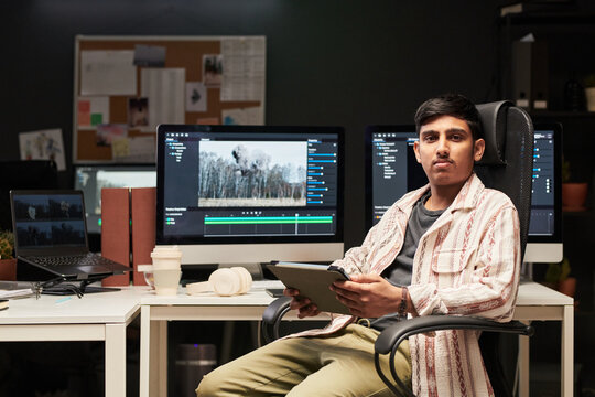 Portrait of Asian gen Z man holding tablet while managing video editing workflow at creative workstation. Useful for digital media, content production, creative careers marketing