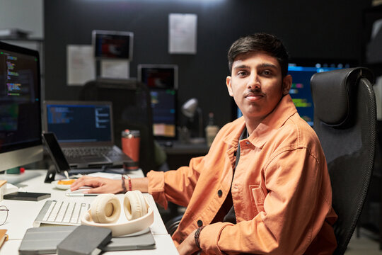 Portrait of young Asian man coding at workstation, looking at camera in software development office. Useful for IT careers, programming services, tech recruitment