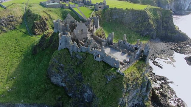 Aerial orbiting shot of Dunluce Castle ruin perched on a dramatic cliff overlooking the Atlantic Ocean in Northern Ireland