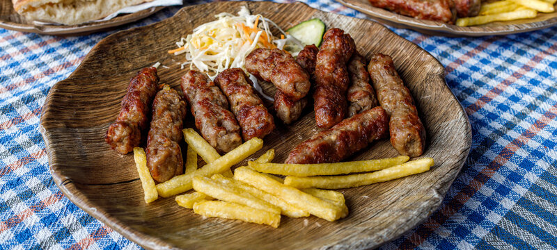Cevapi served with fries and salad on a wooden plate at a local restaurant in the afternoon